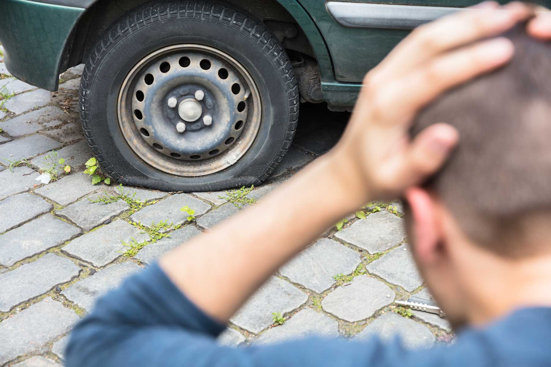 Man looking at a flat tire with his hands on his head